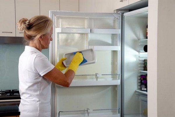 Женщина моет холодильник 