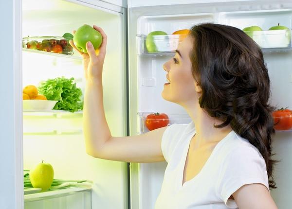Девушка кладет яблоко в холодильник 